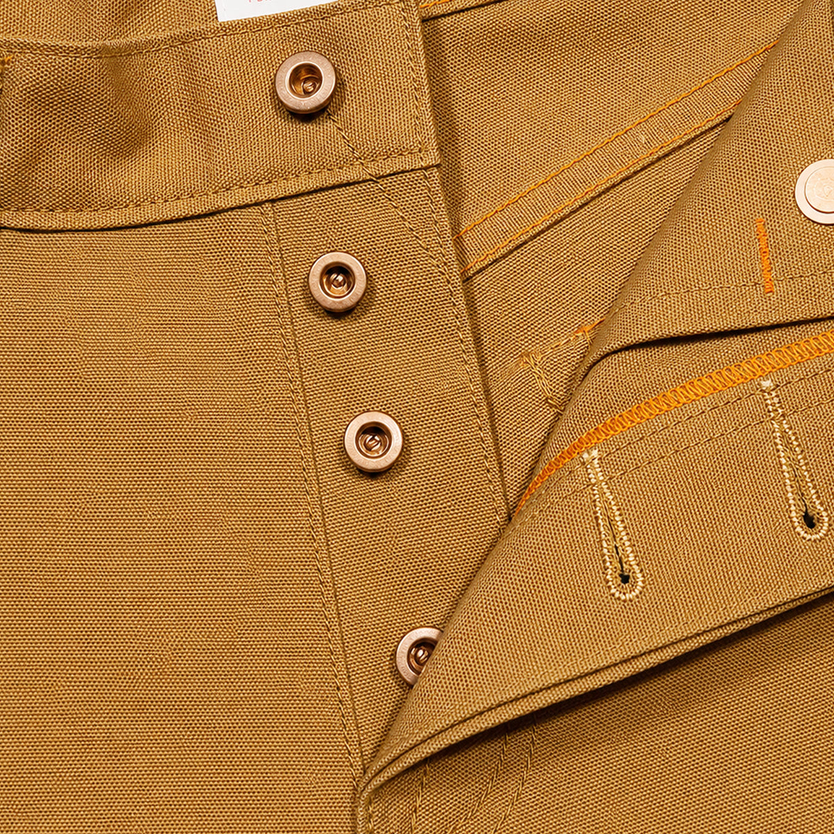 Close-up of a tan canvas garment showing the collar, snap-button placket, and orange contrast stitching details.