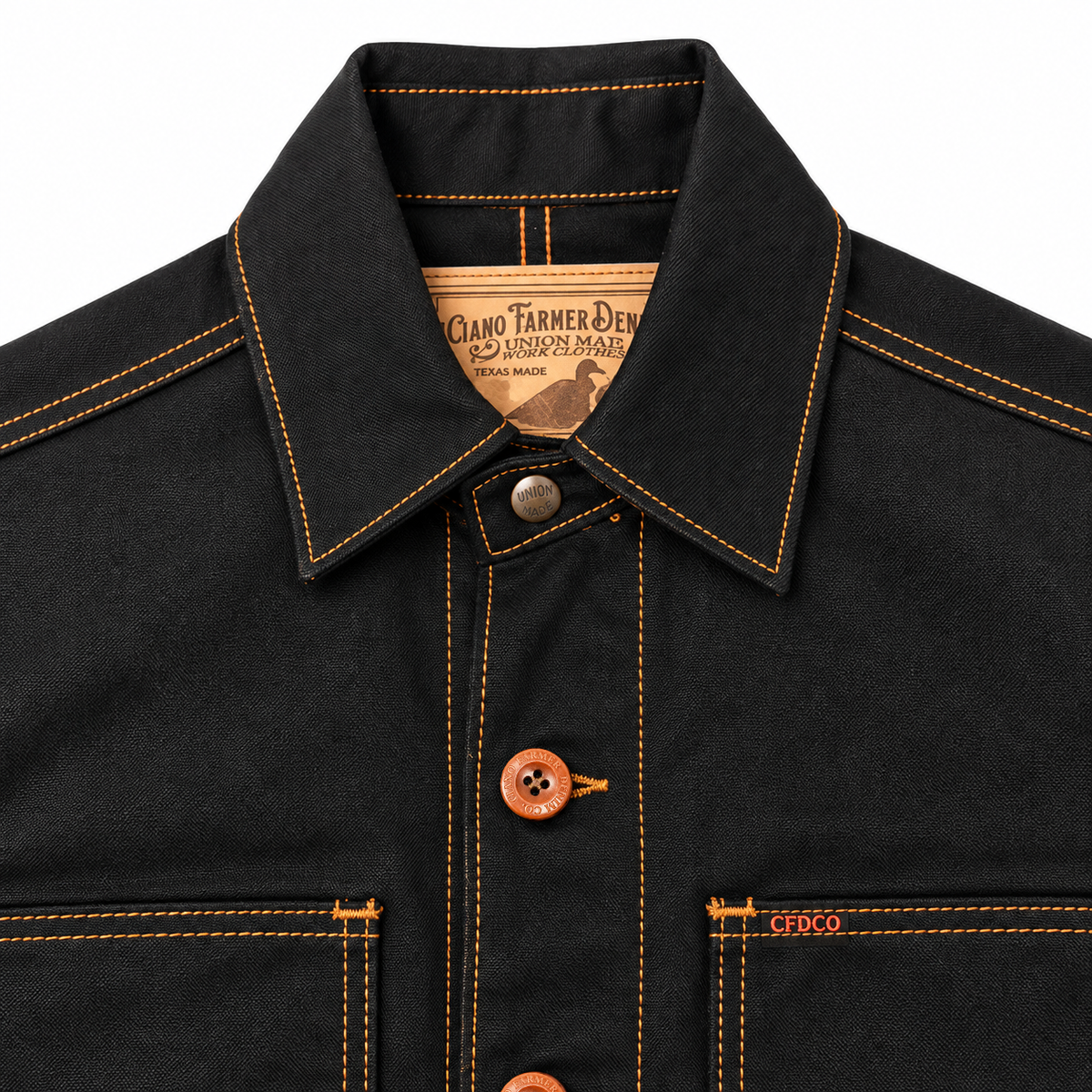Close-up of a dark charcoal gray denim work shirt with orange contrast stitching and orange buttons, featuring a pointed collar and chest pockets.