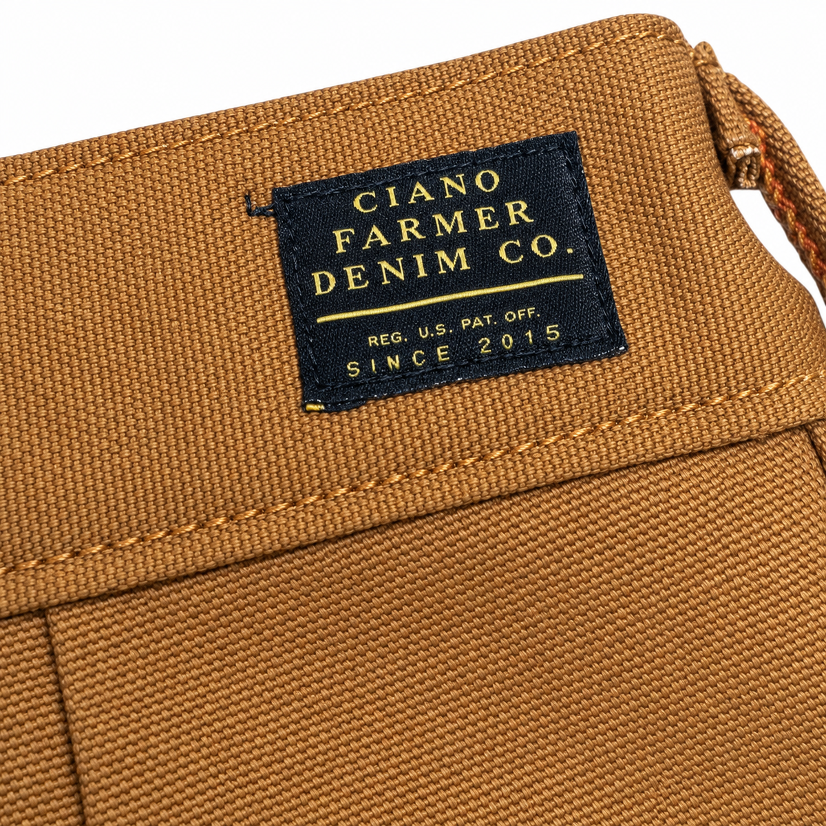 Close-up of a brown canvas bag with a black woven label reading 'CIANO FARMER DENIM CO.' in gold lettering.