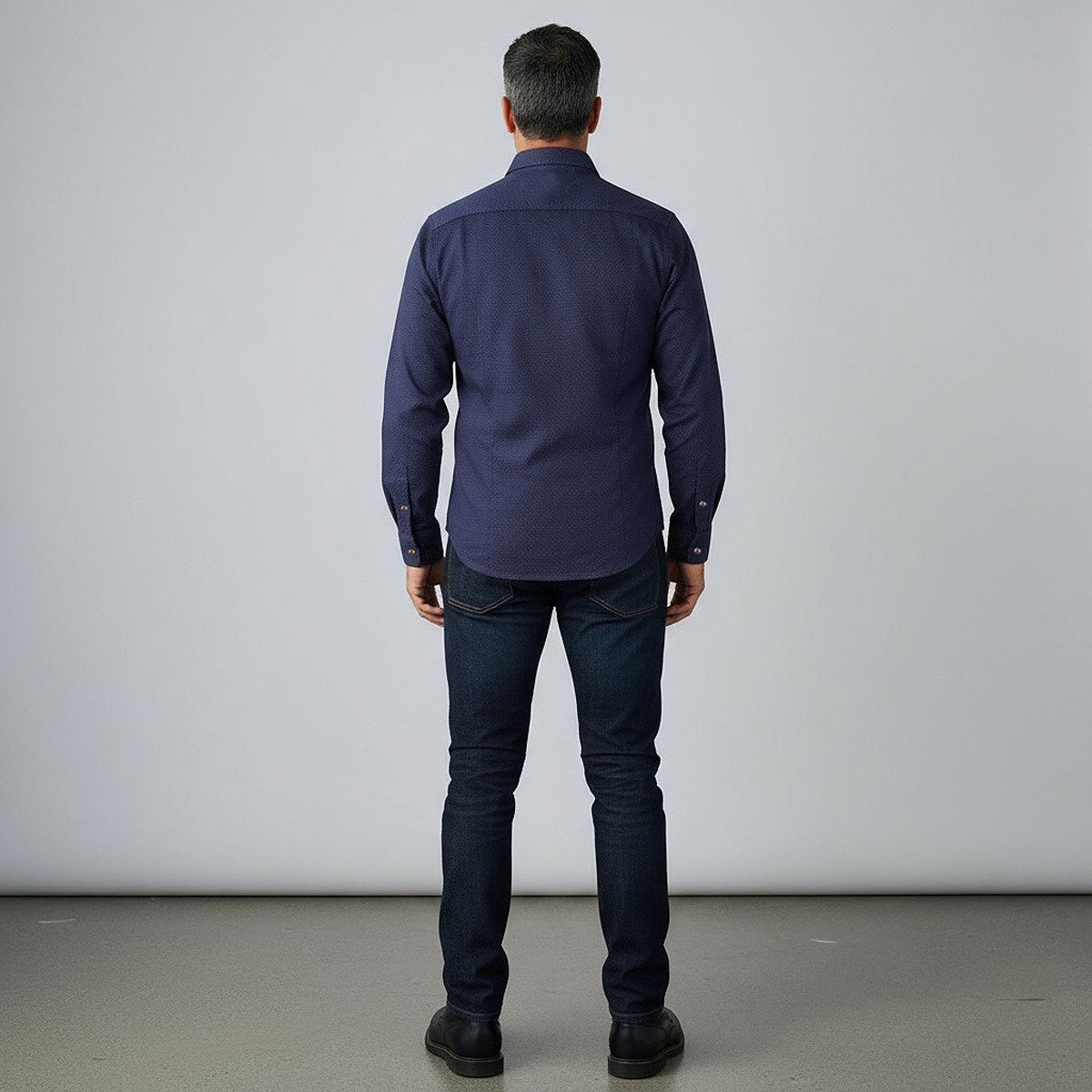 Man wearing a dark blue shirt and jeans standing against a plain white background