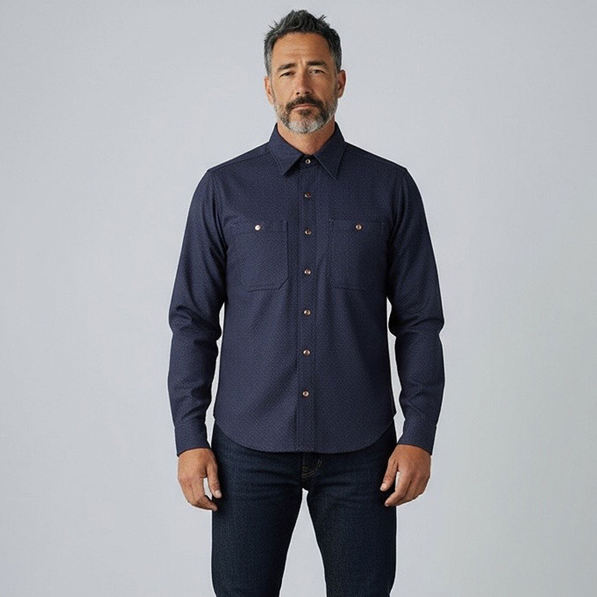 Man wearing a navy button-up shirt and jeans against a plain background