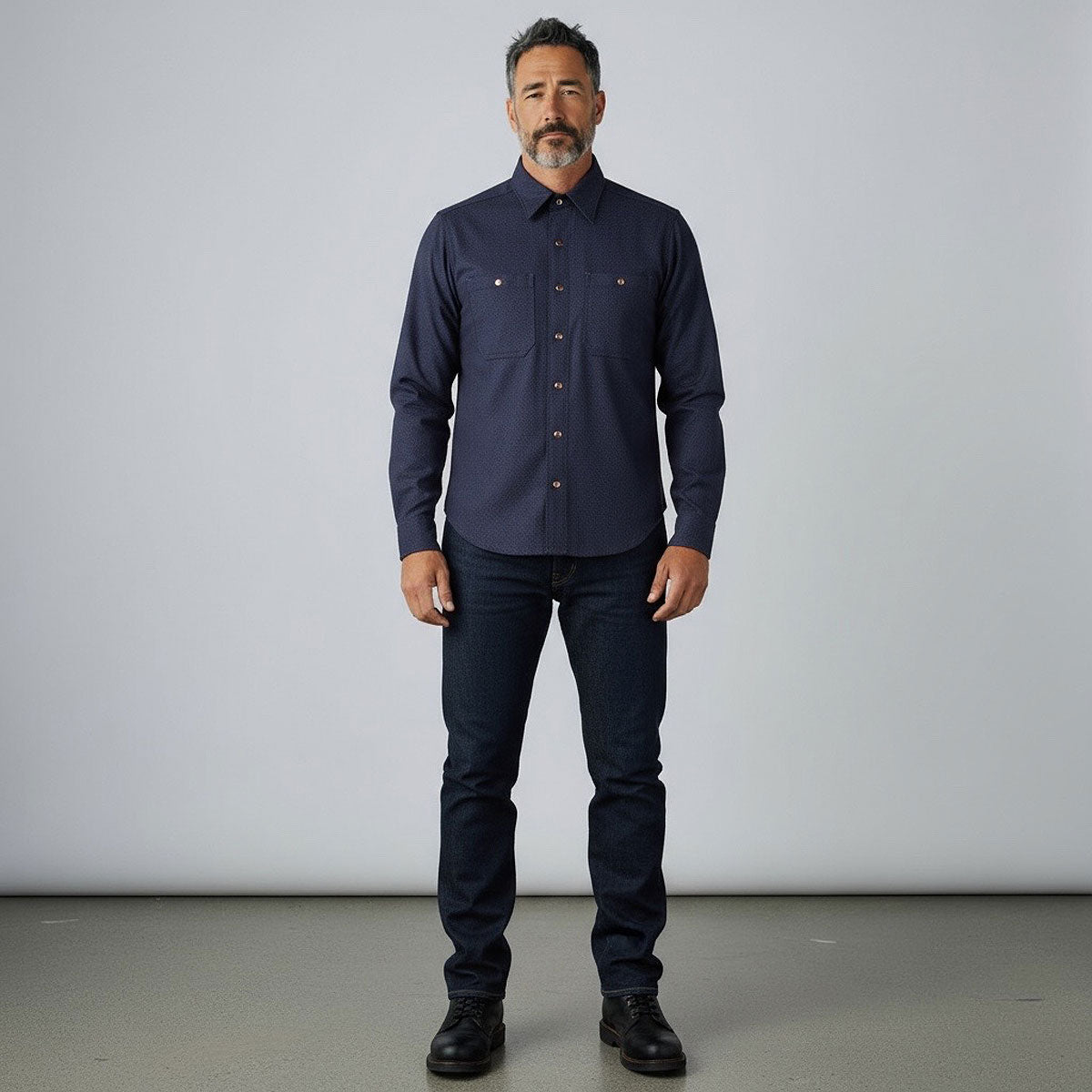 Man wearing a dark blue shirt and jeans against a plain background